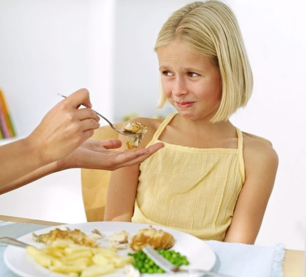 Mother's Hand Feeding Food to a Young Girl (13-14) Who Is Making a Face