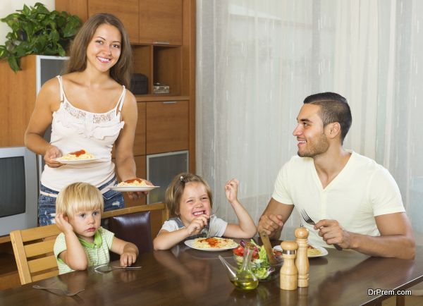 Happy ordinary family of four eating spaghetti at home interior