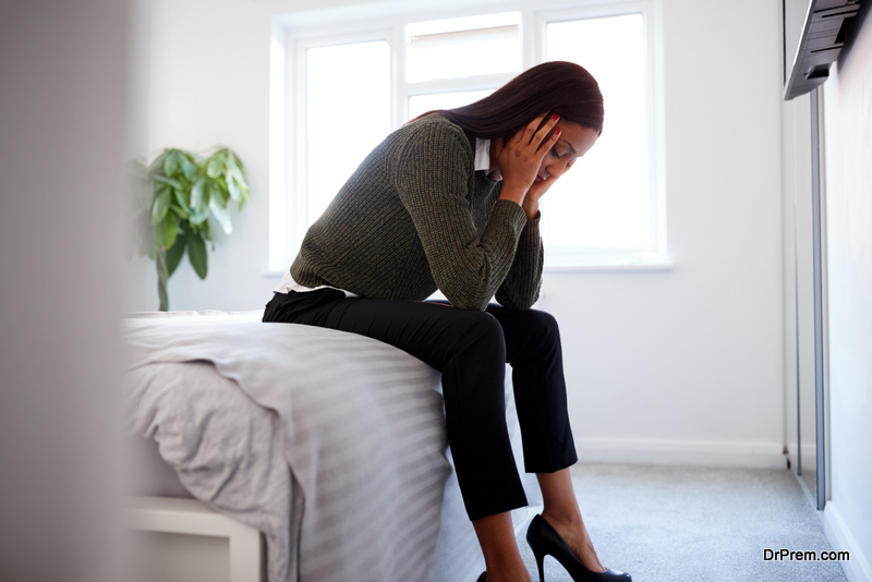 Stressed Businesswoman With Head In Hands Sitting On Edge Of Bed At Home