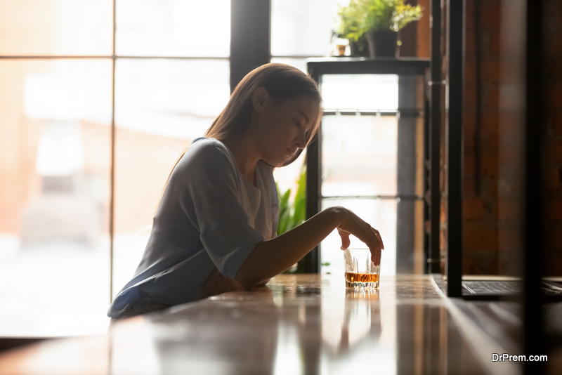 Young sad woman sitting on bar counter drinking alcohol drinks