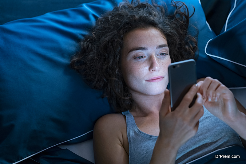 Top view of young woman using a smartphone while lying on bed in the night